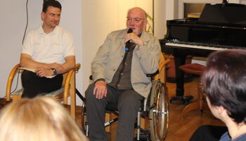 Ein älterer Mann im Rollstuhl hat ein Mikrofon in der Hand und spricht etwas | © Altenheim Marienstift Dachau