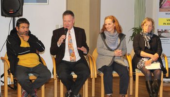 Ein Mann mit Anzug und Krawatte neben einem weiteren Mann und zwei Frauen, spricht in ein Mikrofon | © Altenheim Marienstift Dachau